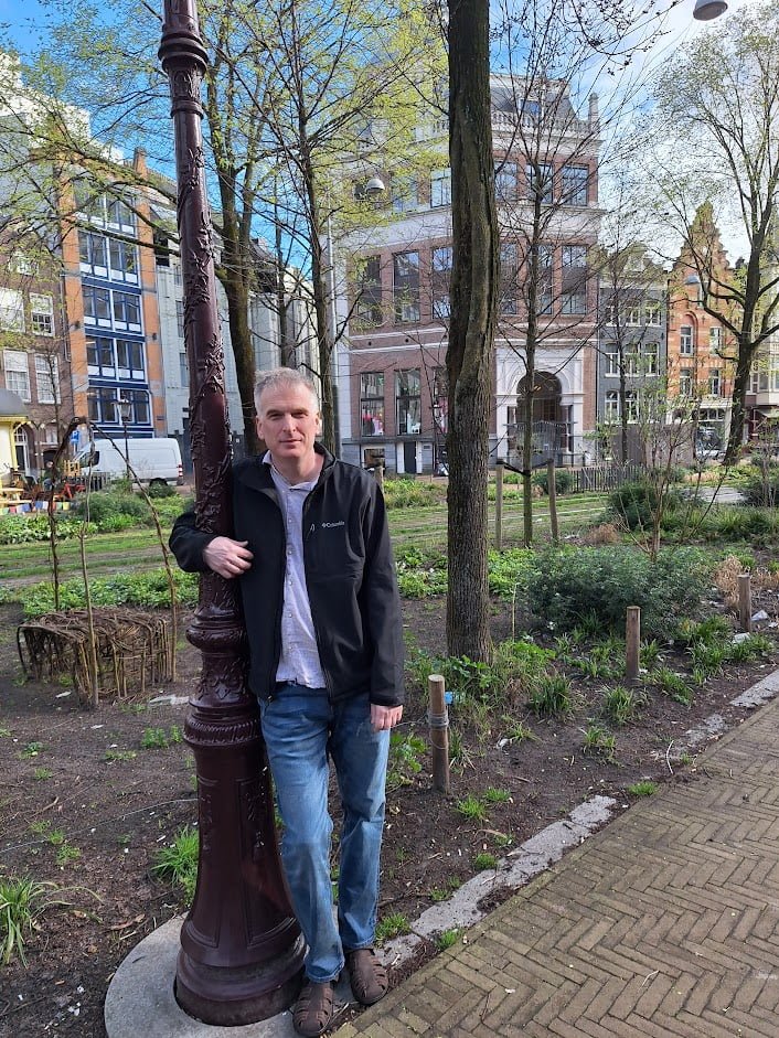 Justin Smith from Vancouver, BC visiting Amsterdam with brick buildings and trees in the background.