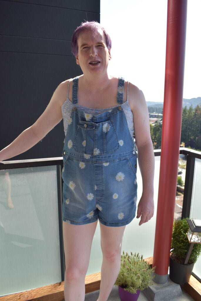 Exposed Sissy in flower overalls standing outside.