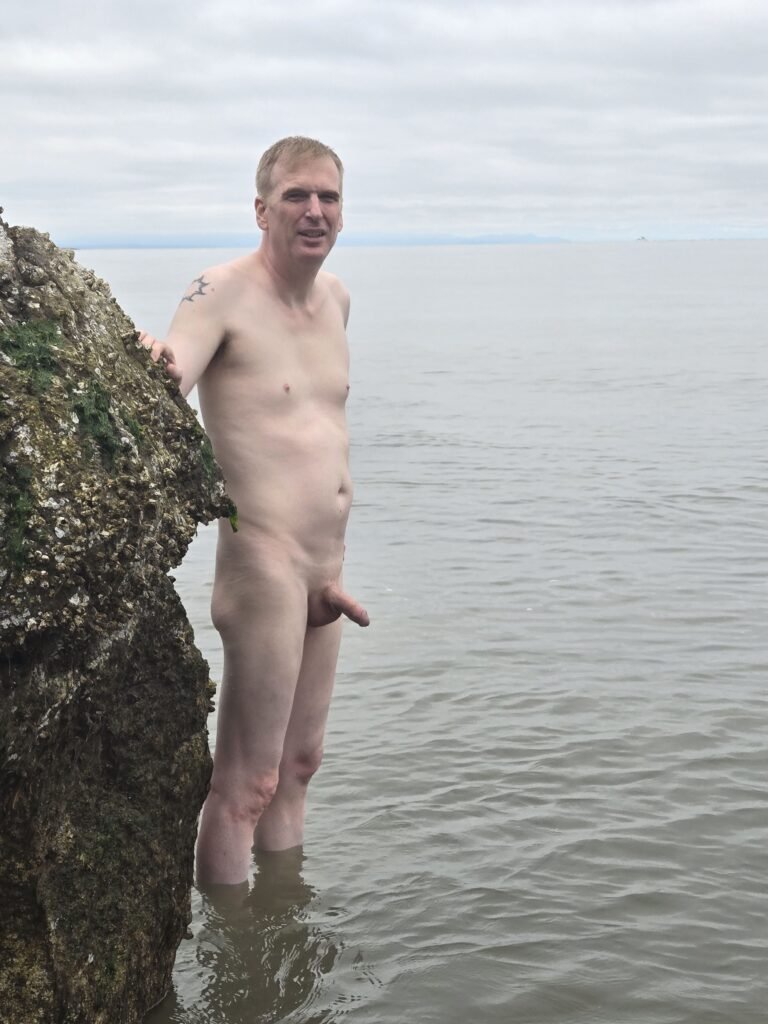 naked man standing in ankle deep water at Wreck Beach in Vancouver.