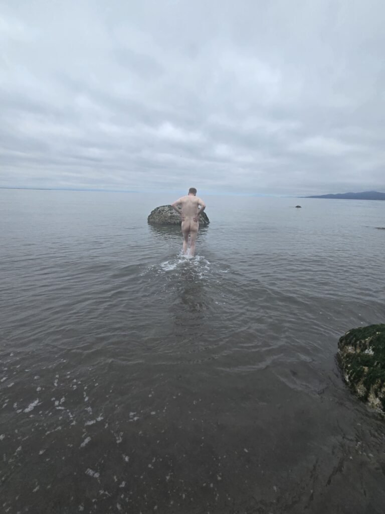 naked man walking in the water at the beach.