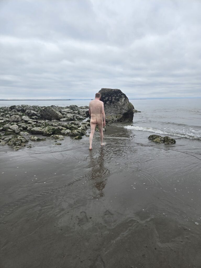 man walking naked on beach on a cloudy day.