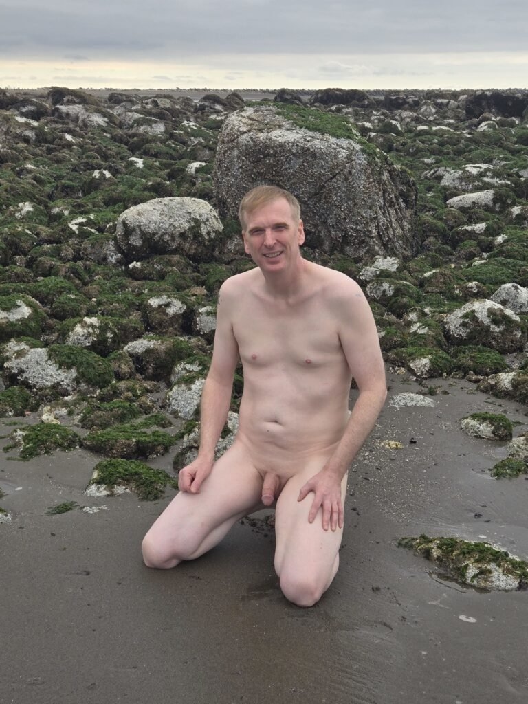 Naked man kneeling on wreck beach in Vancouver.