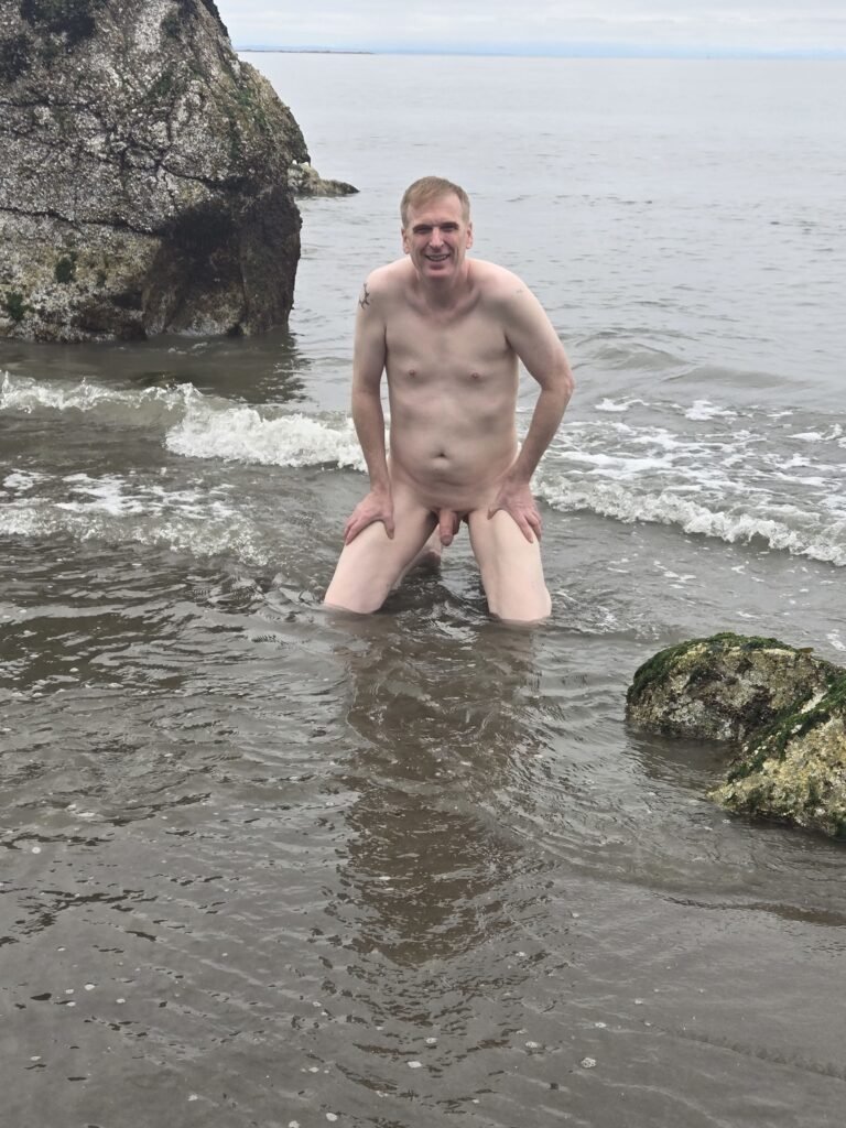 Naked man kneeling in the water on a nude beach in Vancouver.