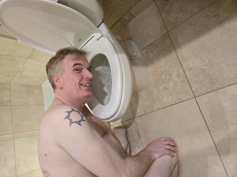 gay bdsm slave kneeling naked in hotel bathroom posing with his head in the toilet.