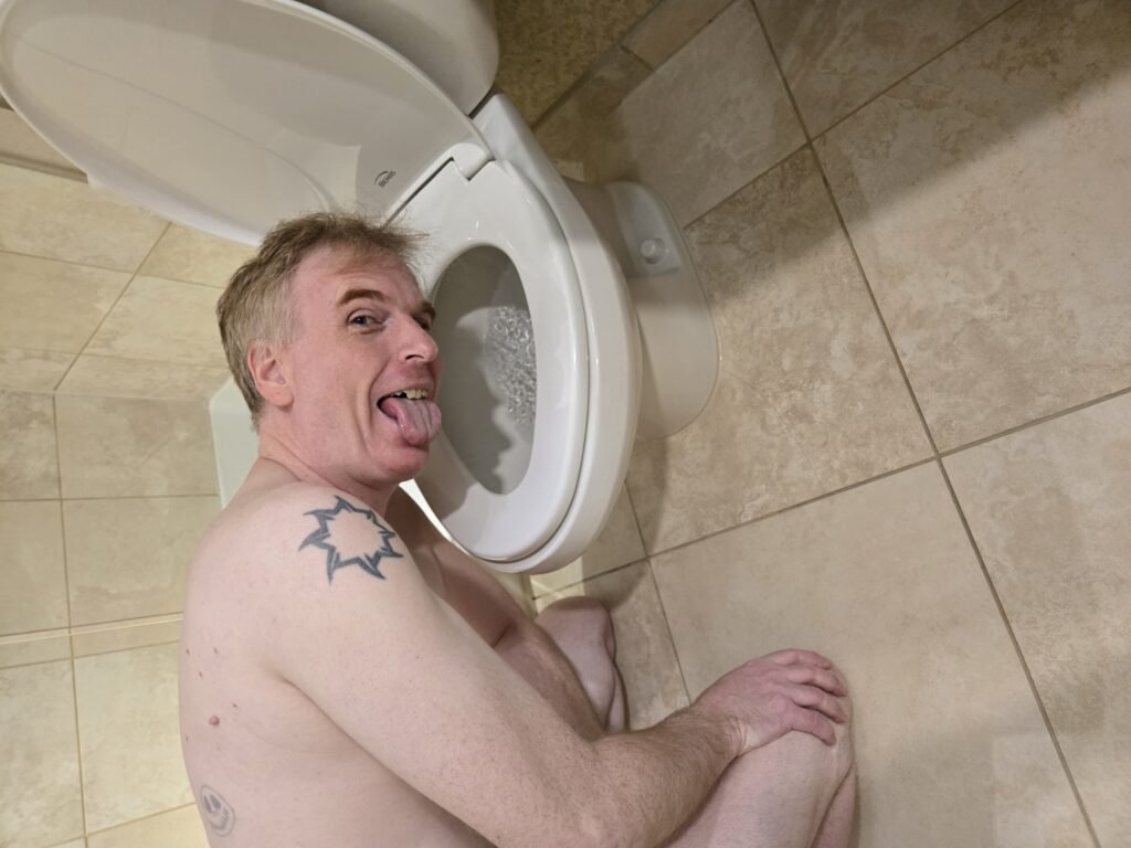 exposed fag kneeling naked by hotel toilet sticking is tongue out.