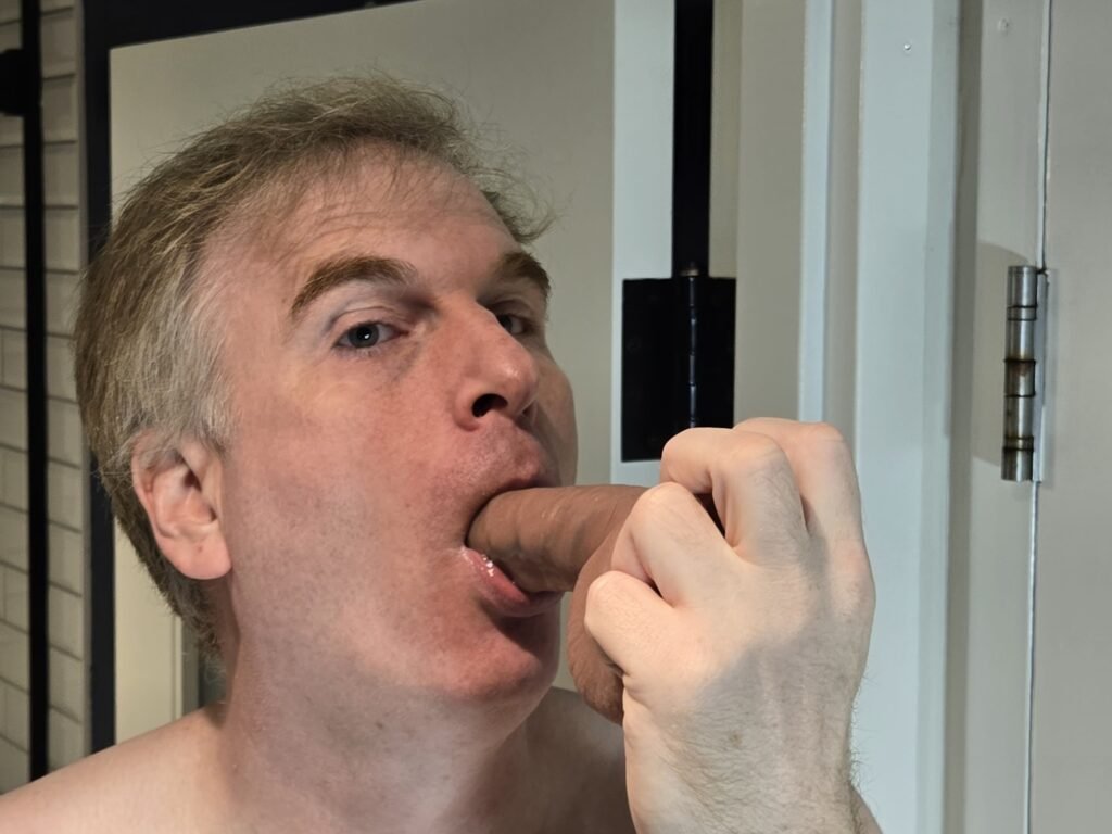 head shot of a male bdsm slave sucking a dildo.