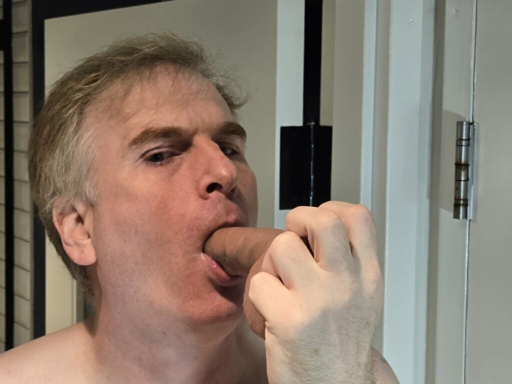 head shot photo of a gay male submissive sucking a dildo.