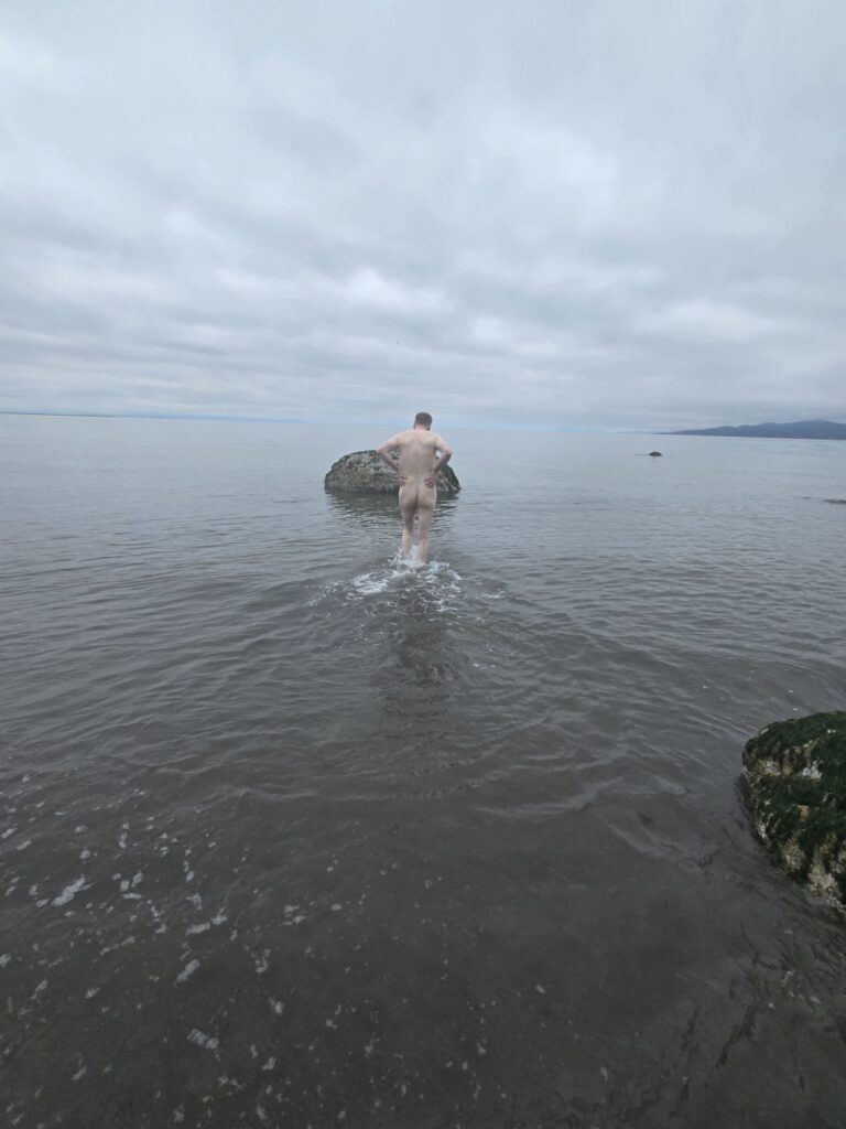 man walking in the water at a nude beach.